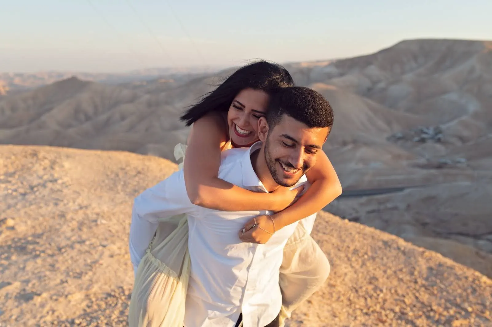 בחורה רכובה על גב בן זוגה, צוחקים במדבר
