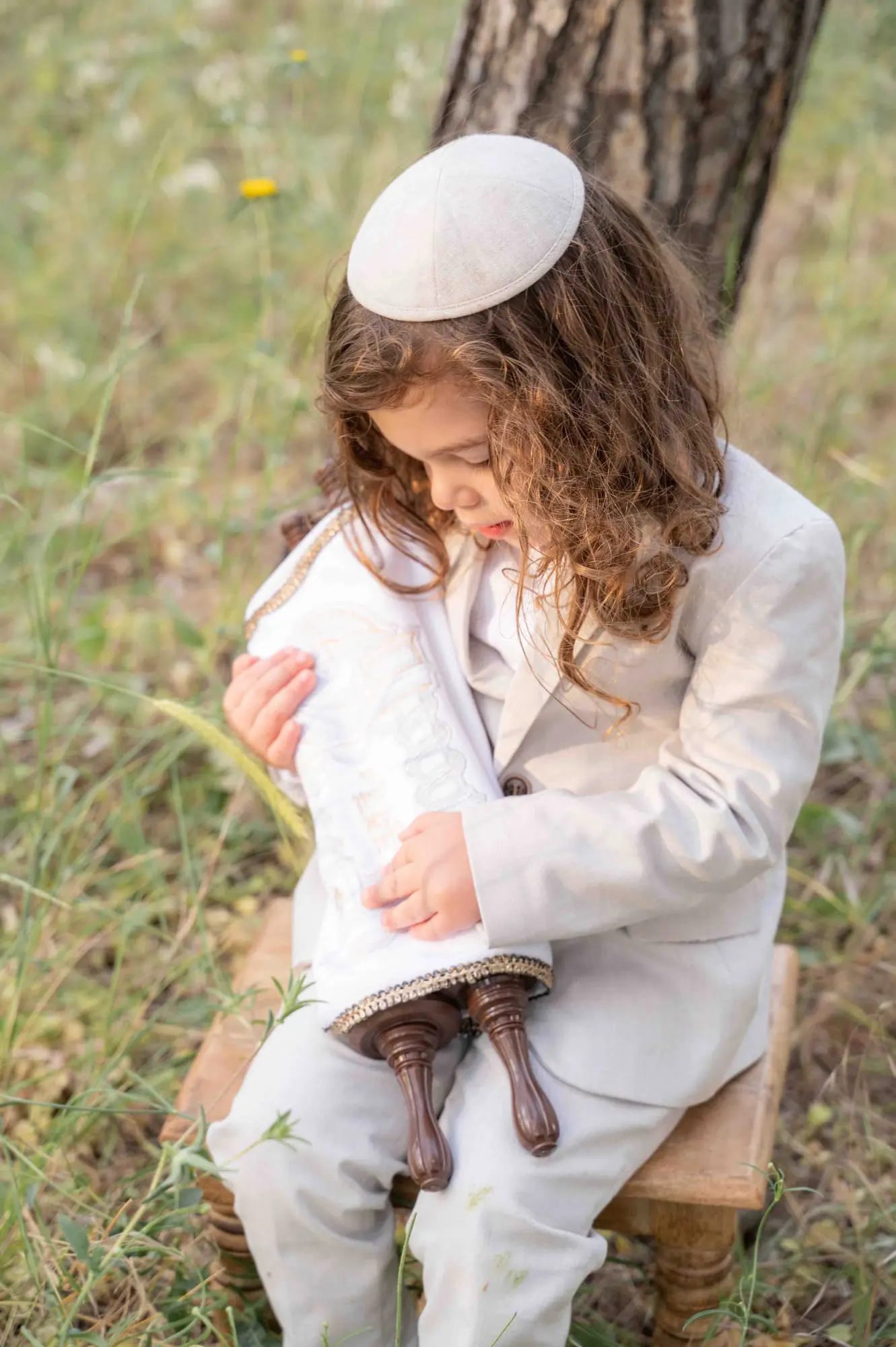 ילד מחבק ספר תורה בחליפה בהירה