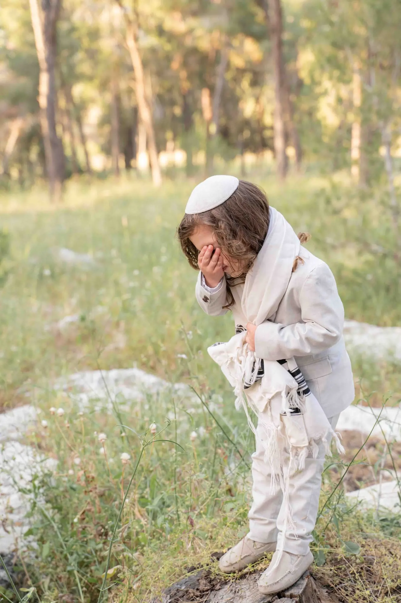 ילד מסתיר צחוק מאחורי ידו, עטוף בטלית