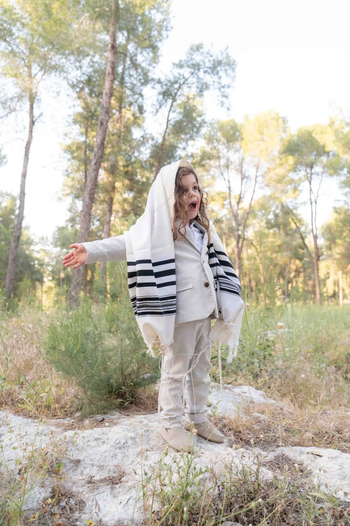 ילד עטוף בטלית פורש זרועות בשמחה בשדה