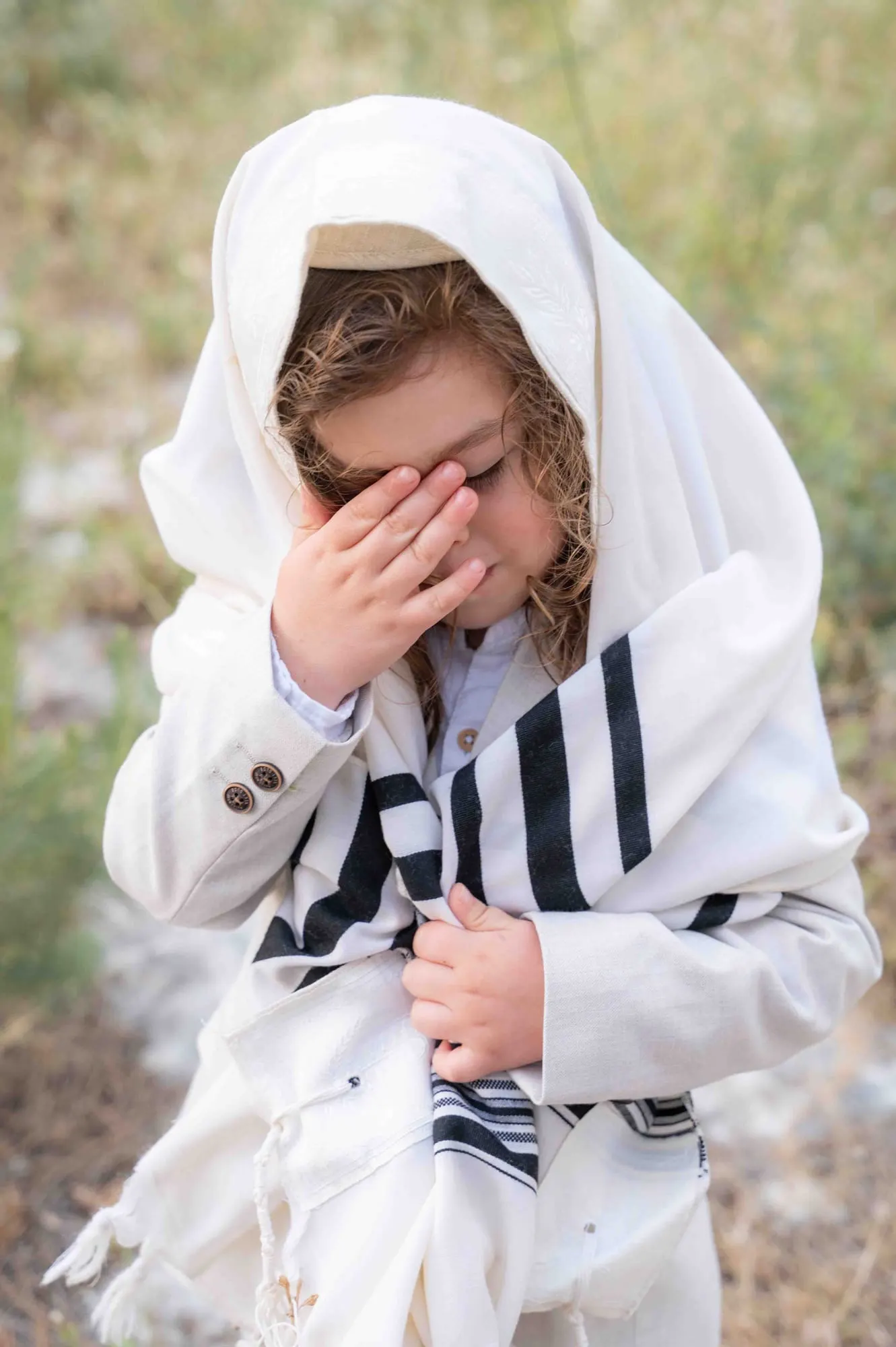 ילד עטוף בטלית מכסה את עיניו בתפילה