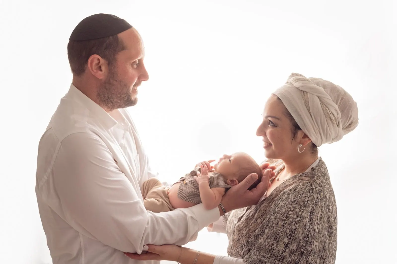 הורים מביטים זה בזה ומחזיקים יחד את תינוקם, רקע לבן בהיר